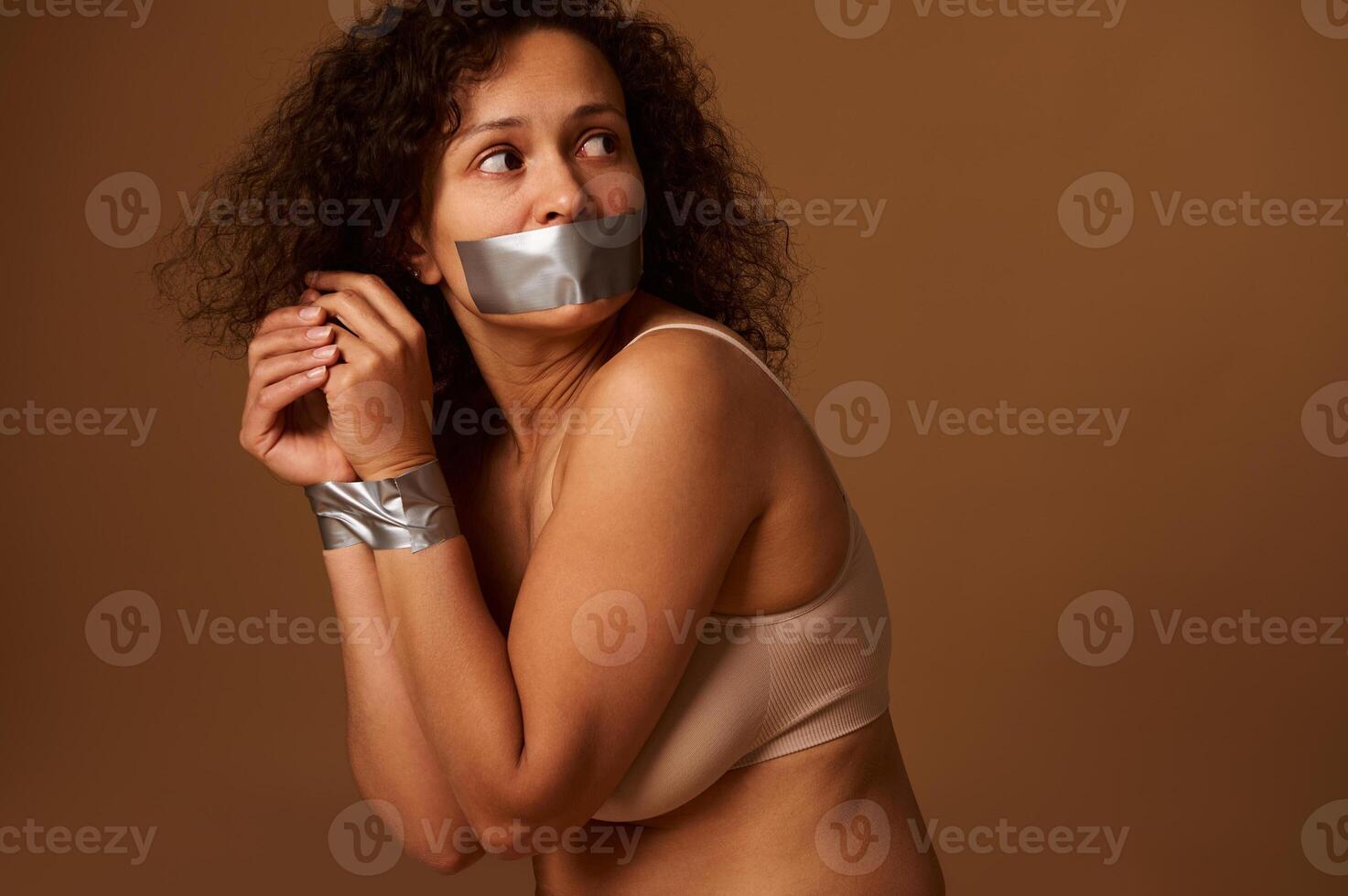 Close up portrait of frightened desperate woman with her mouth closed and her hands tied, looking back with hope and praying for help in ending violence against women. Social concept, dark background photo