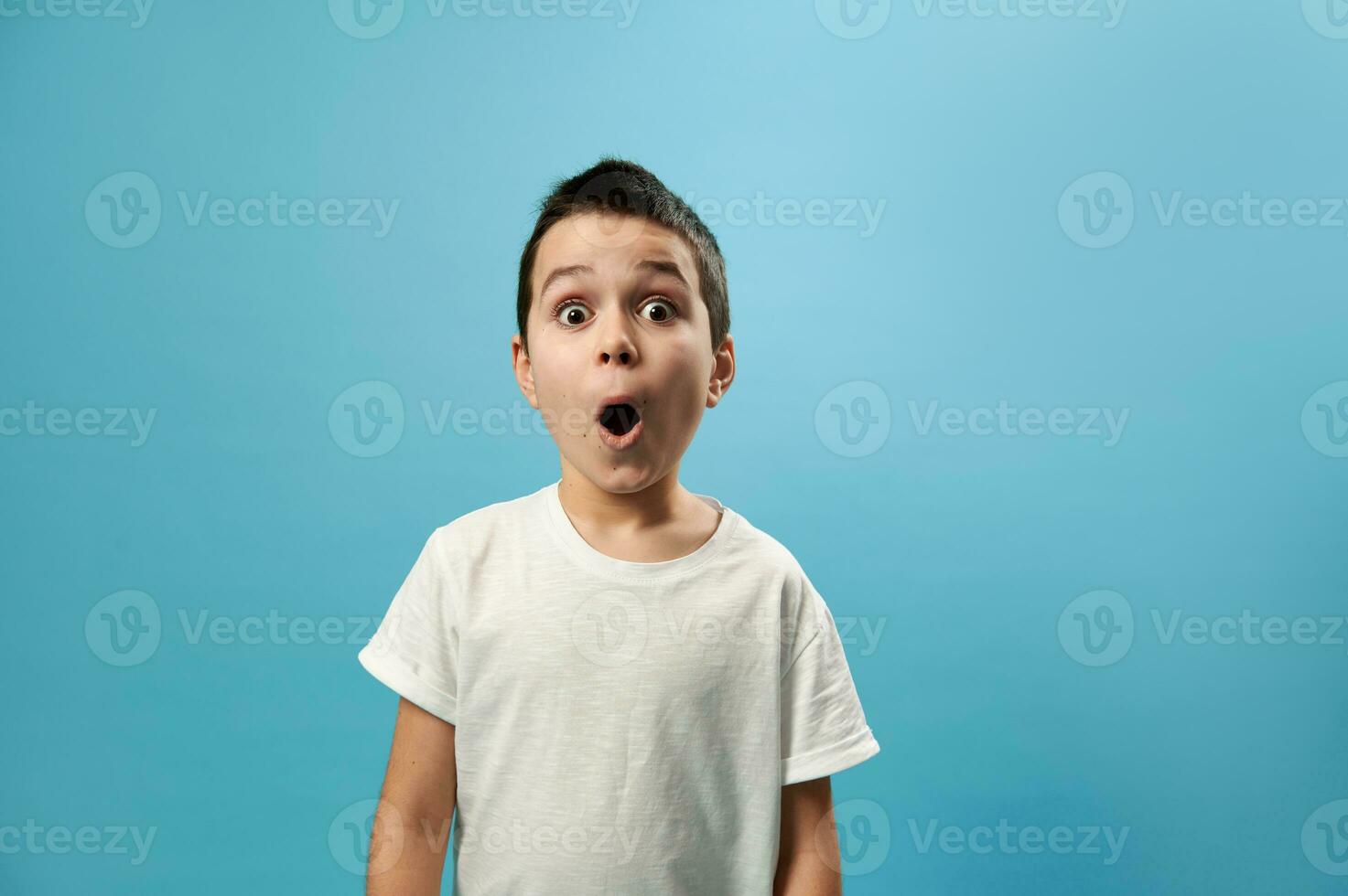 Shocked boy posing with opened mouth expressing surprise on blue background with copy space photo