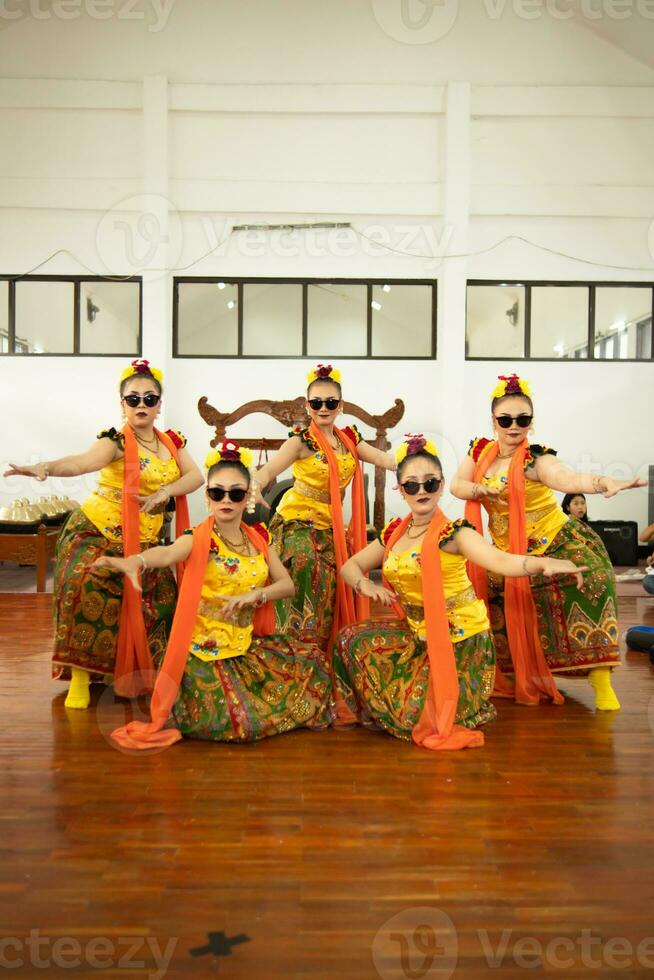 a group of traditional Javanese dancers dancing very agile while wearing sunglasses and yellow costumes on stage photo