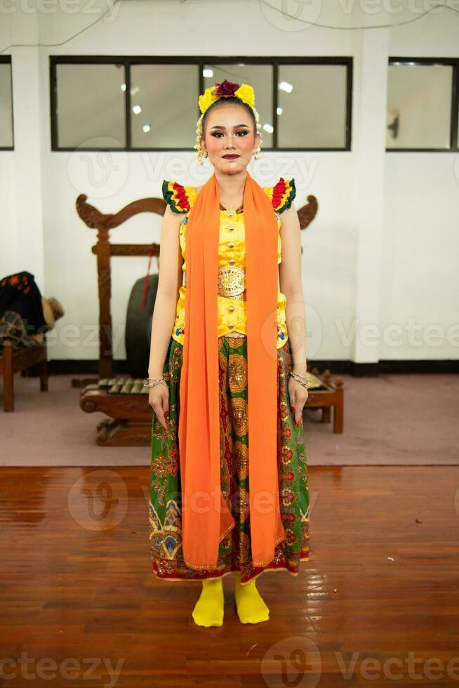 un tradicional indonesio bailarín en pie en un amarillo disfraz y un naranja bufanda colgando abajo su cuerpo foto