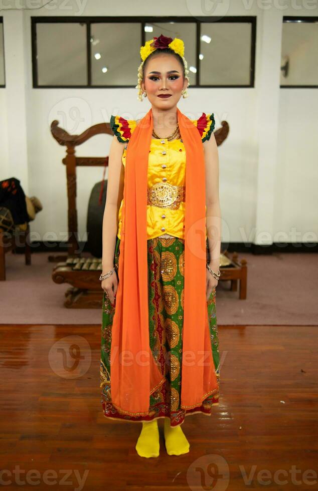 un tradicional indonesio bailarín en pie en un amarillo disfraz y un naranja bufanda colgando abajo su cuerpo foto