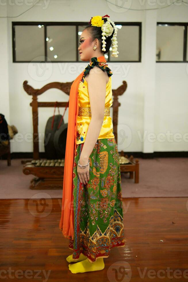 a traditional Indonesian dancer standing in a yellow costume and an orange scarf hanging down her body photo