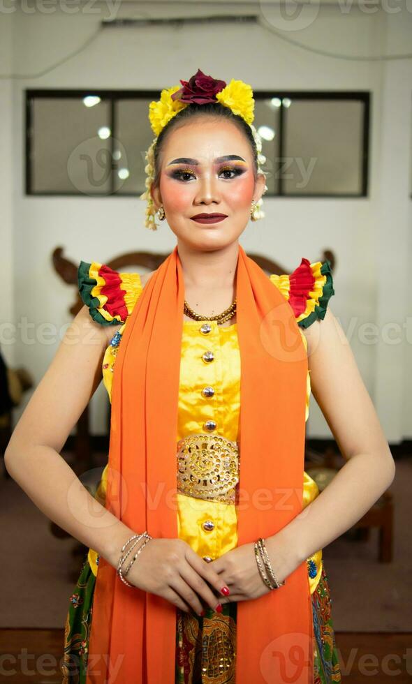 un tradicional indonesio bailarín en pie en un amarillo disfraz y un naranja bufanda colgando abajo su cuerpo foto