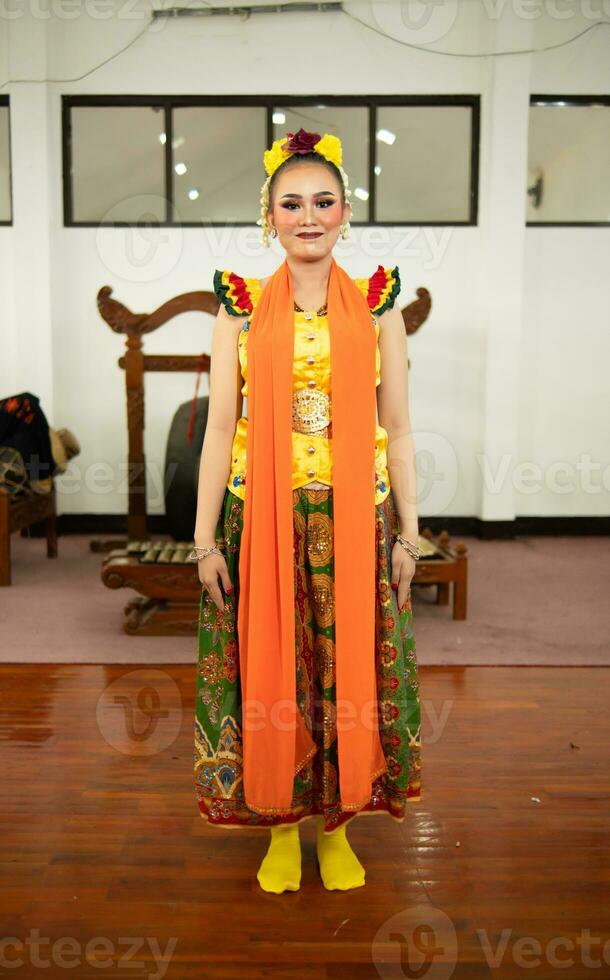 un tradicional indonesio bailarín en pie en un amarillo disfraz y un naranja bufanda colgando abajo su cuerpo foto