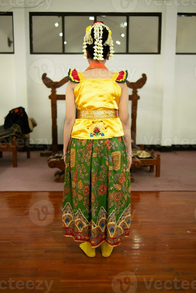 a traditional Indonesian dancer standing in a yellow costume and an orange scarf hanging down her body photo