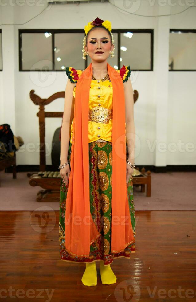 a traditional Indonesian dancer standing in a yellow costume and an orange scarf hanging down her body photo