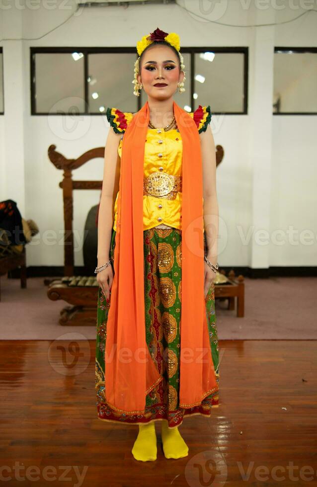 un tradicional indonesio bailarín en pie en un amarillo disfraz y un naranja bufanda colgando abajo su cuerpo foto