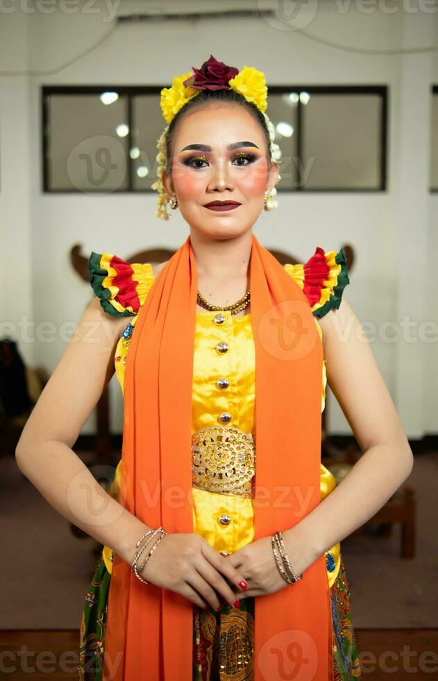 un tradicional indonesio bailarín en pie en un amarillo disfraz y un naranja bufanda colgando abajo su cuerpo foto