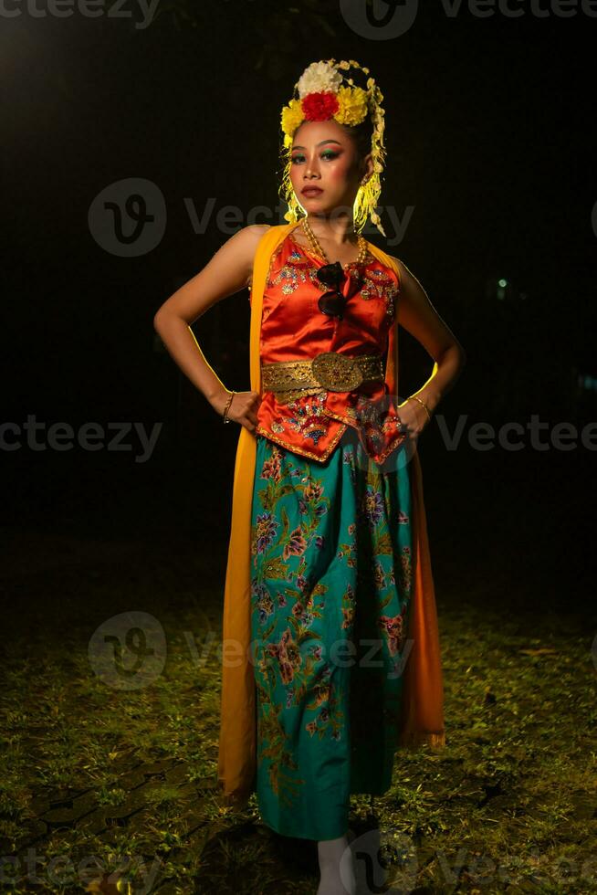 a Javanese dancer poses with sharp eyes and a golden costume on stage photo