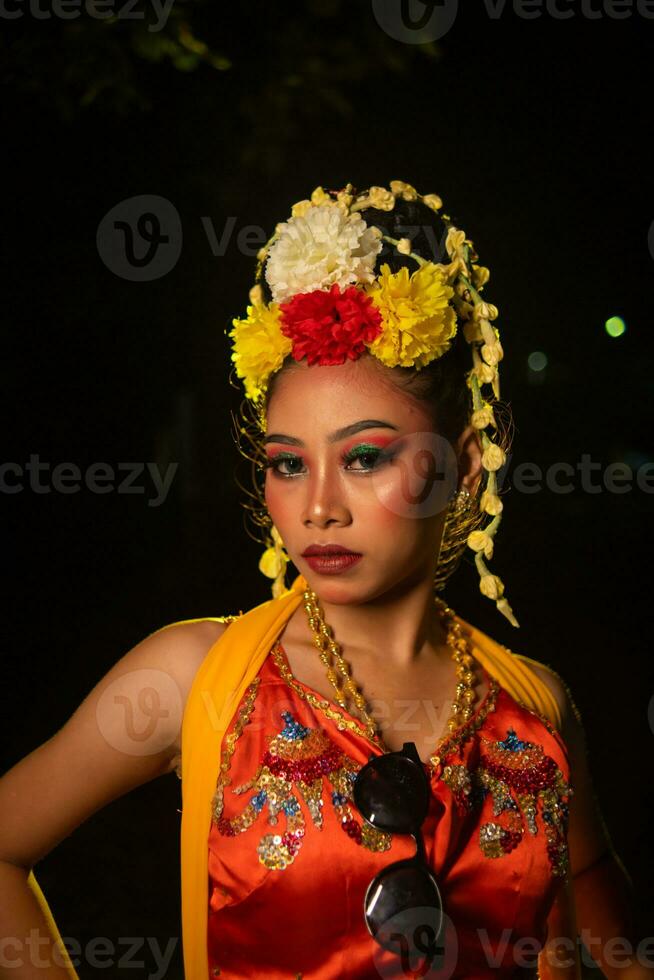 a Javanese dancer poses with sharp eyes and a golden costume on stage photo