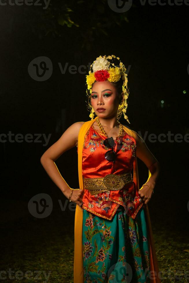 a Javanese dancer poses with sharp eyes and a golden costume on stage photo