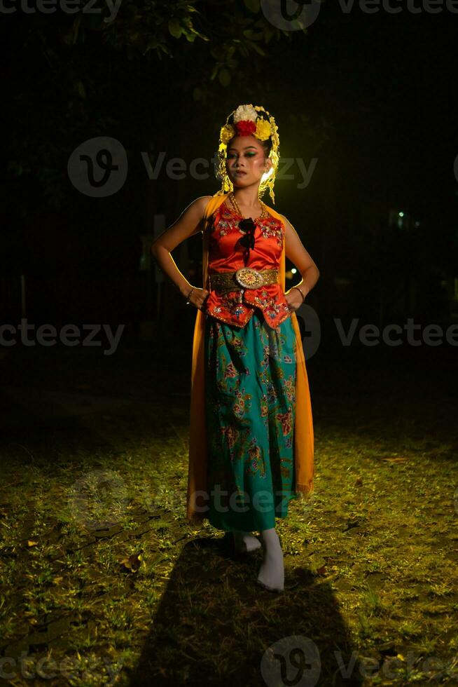 a Javanese dancer poses with sharp eyes and a golden costume on stage photo