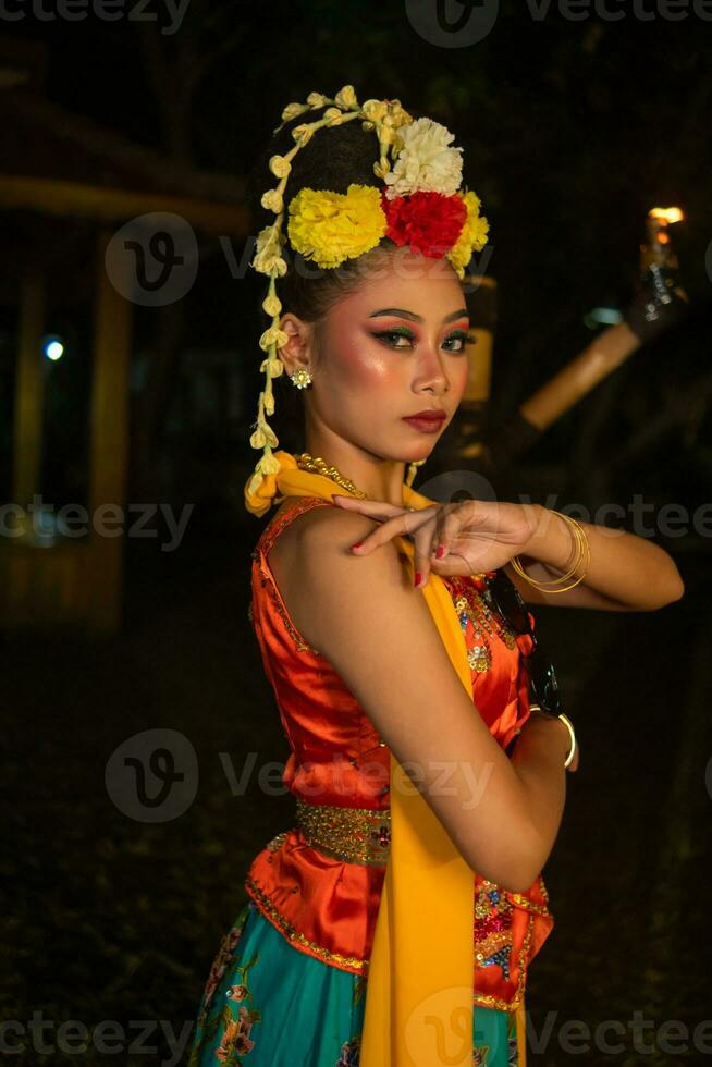 a Javanese dancer poses with sharp eyes and a golden costume on stage photo