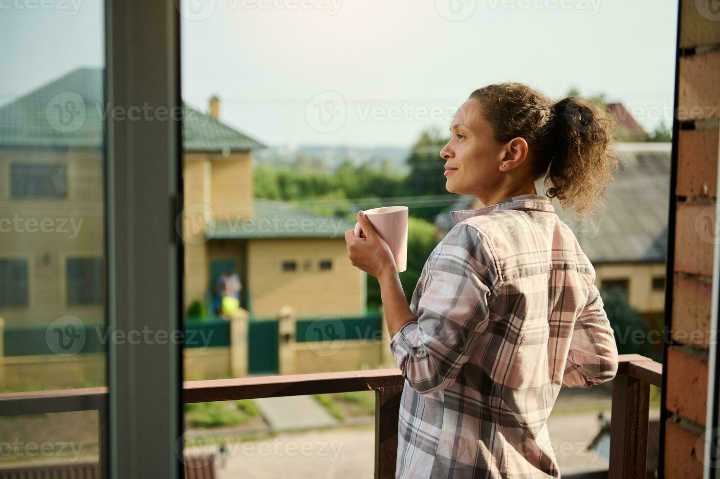 Hispanic pretty woman with a cup of hot drink on balcony of her country house photo