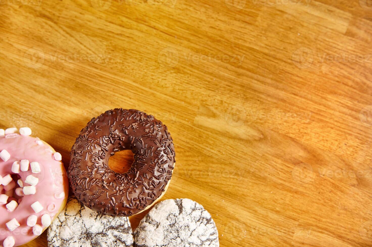 Assorted doughnuts with sprinkles on wooden surface. Background with copy space. photo