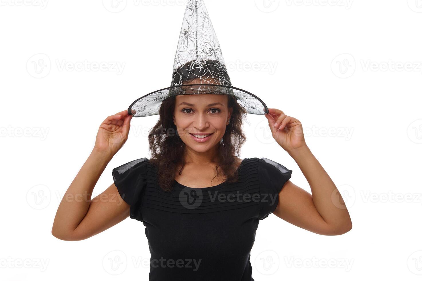 Isolated portrait on white background with copy space for Halloween ad of a beautiful woman smiling with beautiful toothy smile, wearing a witch wizard hat and looking at camera photo