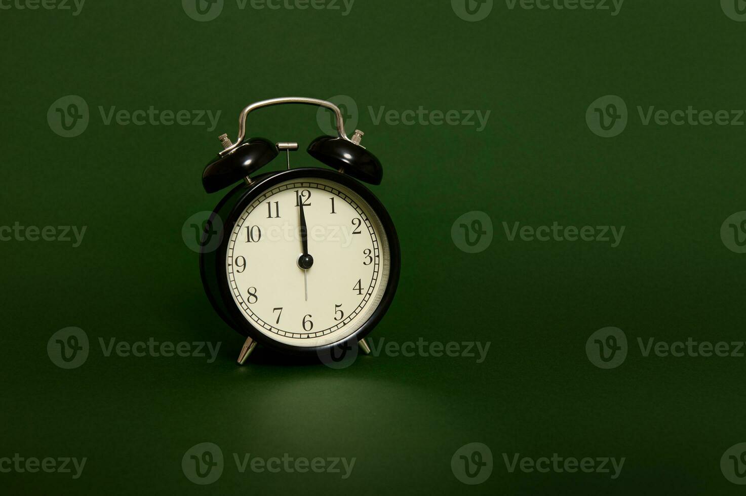 Studio shot with soft shadows of a black alarm clock with midnight on the clock face isolated over dark green background with copy space for ad. Time to celebrate Christmas and New Year photo