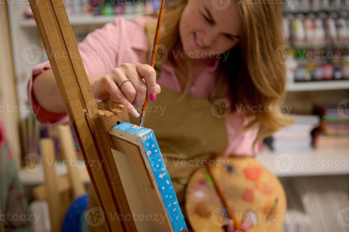 Focus on hand of female painter holding paint brush, drawing picture on canvas, standing at wooden easel in her workshop photo