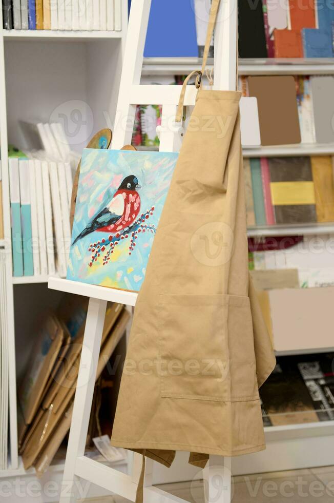 Still life. An oil painting is displayed on a white wooden easel with an apron in creative workshop. Hobby. Art painting photo