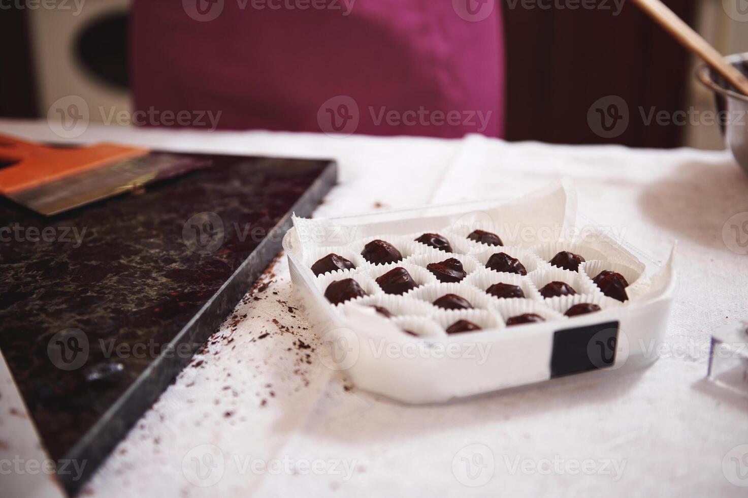 Box full of handmade chocolate truffles and bonbons on a white tablecloth next tp marble surface with a scraber on it photo