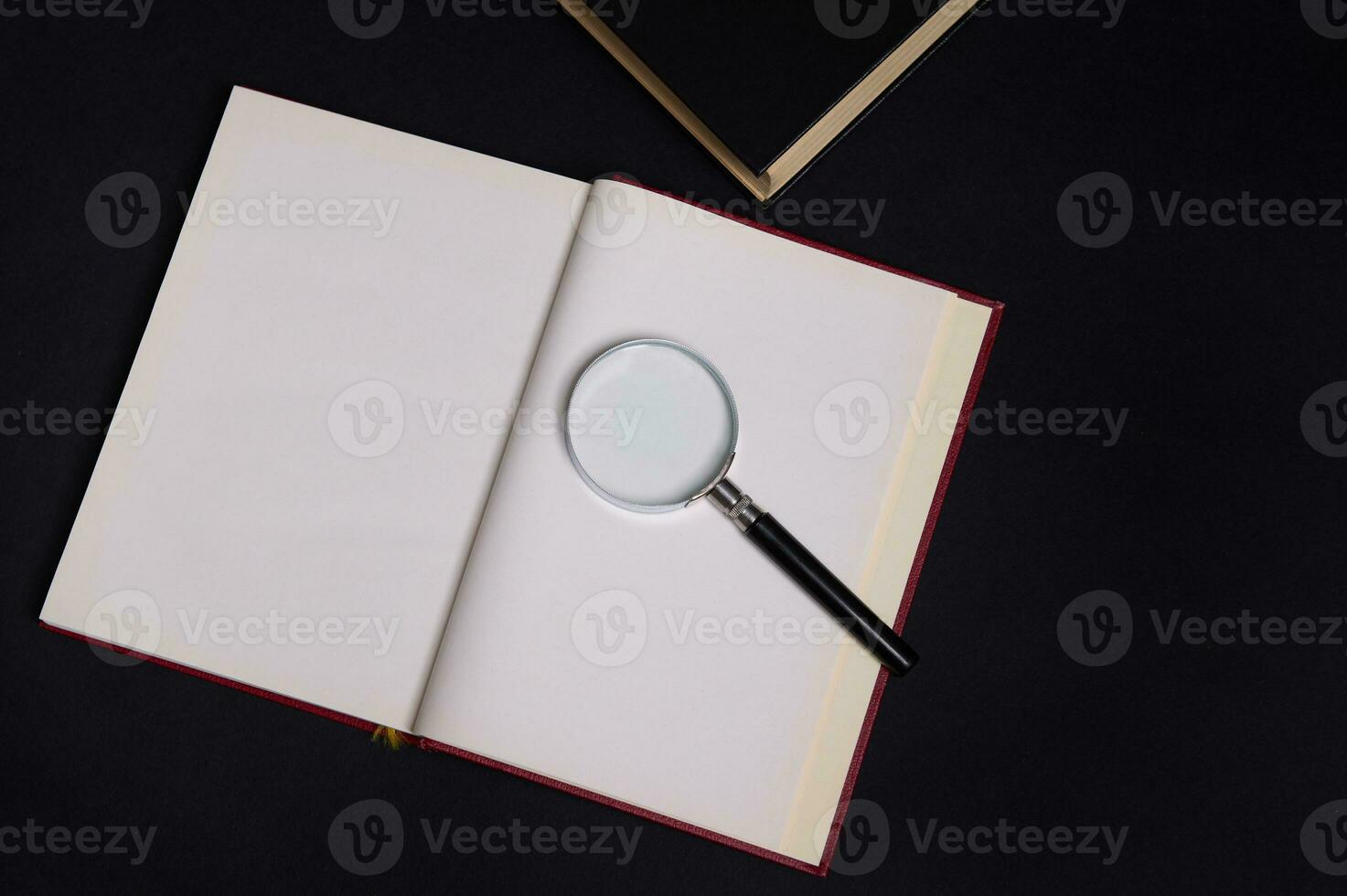 Flat lay composition of a magnifying glass on an opened book in hard red cover, isolated over black background with space for text. Teacher's Day concept, Knowledge, literature ,reading, erudition photo