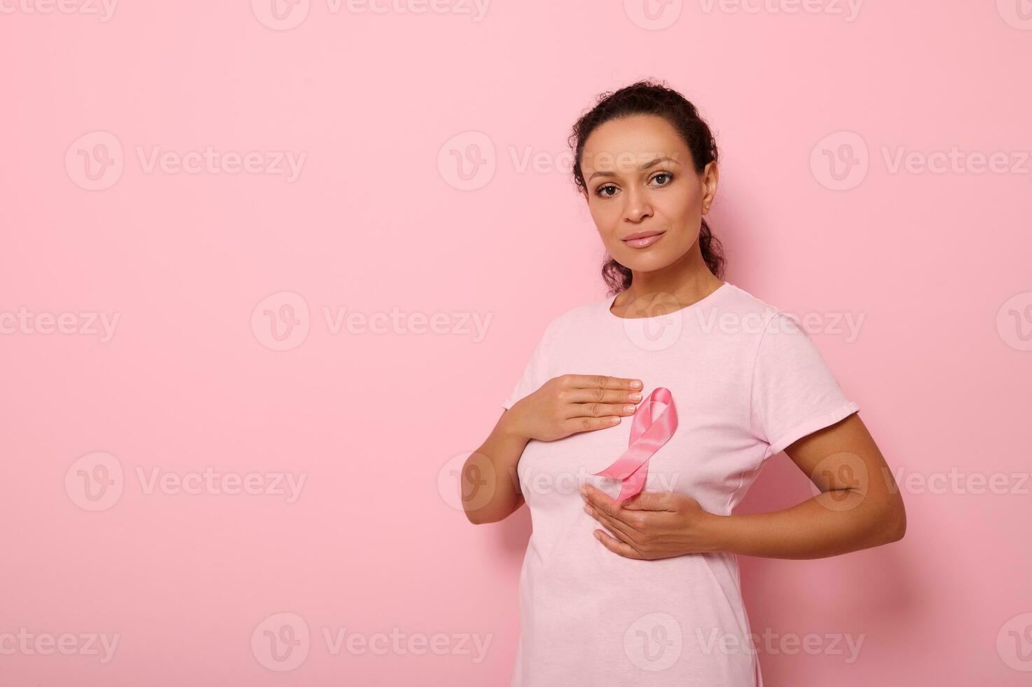 African American woman puts hands around pink ribbon on her pink T Shirt, for breast cancer campaign, supporting Breast Cancer Awareness. Concept of 1 st October Pink Month and women's health care photo