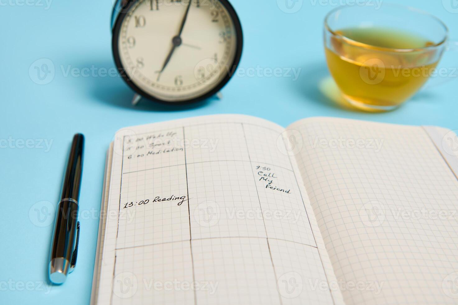 Time management, deadline and schedule concept. Alarm clock on schedule plan, organizer with plans, ink pen and transparent glass cup with tea on blue background with space for text photo