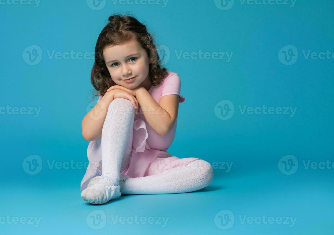 adorable preescolar niña niño, ballet bailarín, posando a el cámara, sentado terminado azul antecedentes. foto