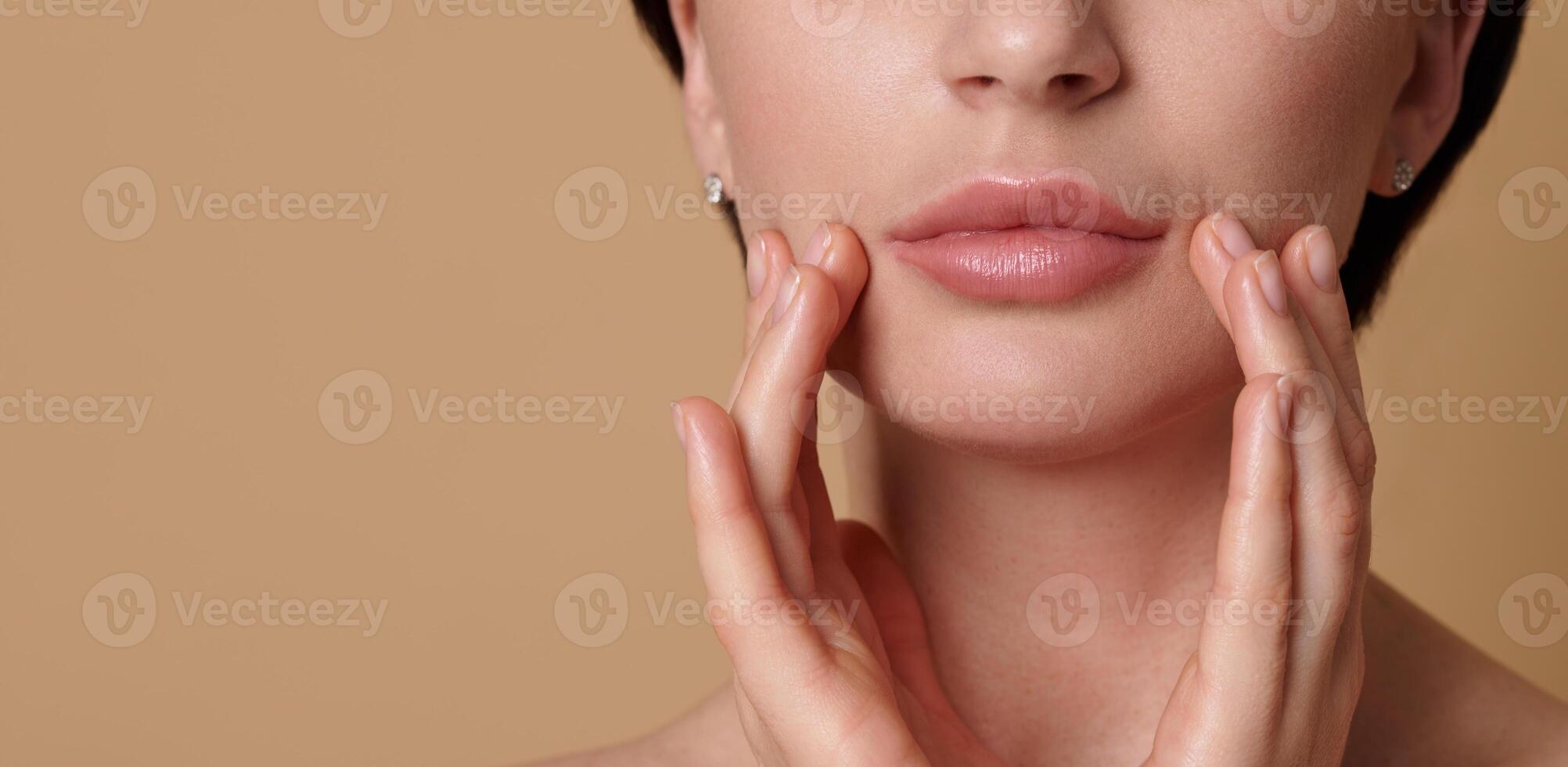 Close-up cropped beauty face portrait of beautiful European woman touching her perfect clean fresh and shiny skin near her lips. Skin care, cosmetology, SPA concept on beige background, copy space photo