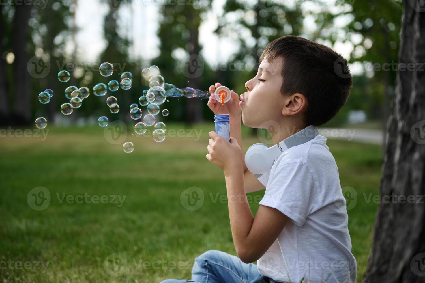 Adorable handsome preadolescent child boy blowing starting soap bubbles on the park, resting during his school recreation photo