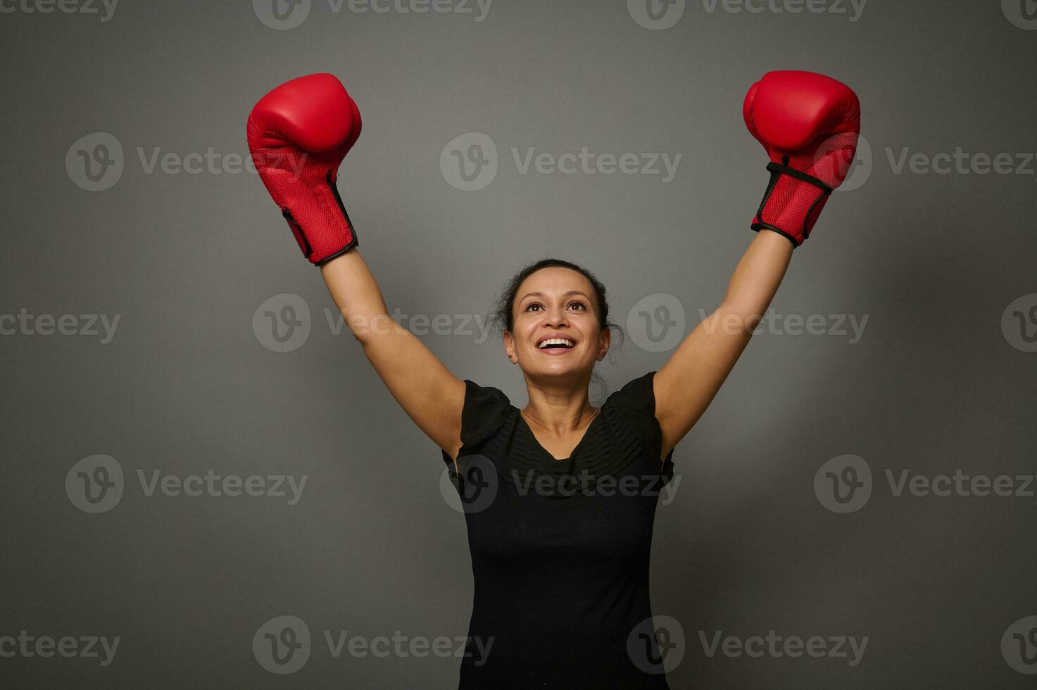 Concept of blow to prices on gray background with copy space. Woman boxer in black medical protective mask and boxing gloves raises hands in winner position. Shooting for boxing day and black friday photo