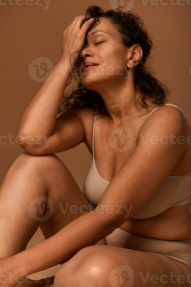 bonito mujer con imperfecto cuerpo, celulitis y tramo marcas vistiendo beige ropa interior ocultación medio de su cara posando en contra de colores antecedentes con Copiar espacio foto