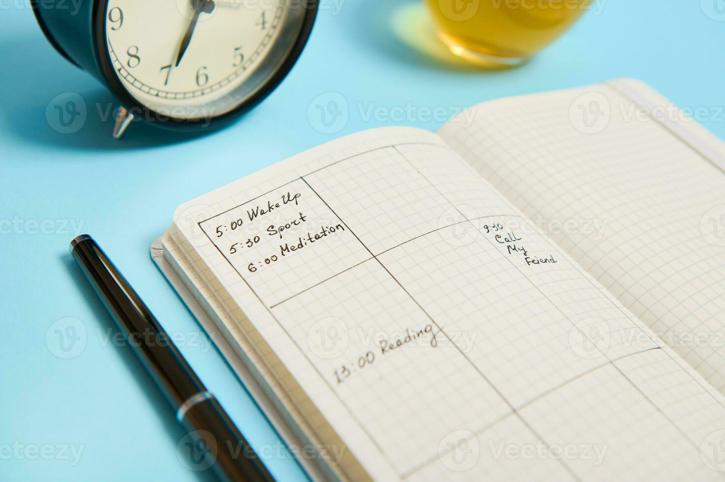 Cropped image of an open notebook with schedule, ink pen, black alarm clock lie on blue surface. Color background with copy space. Time management, deadline and schedule concept photo