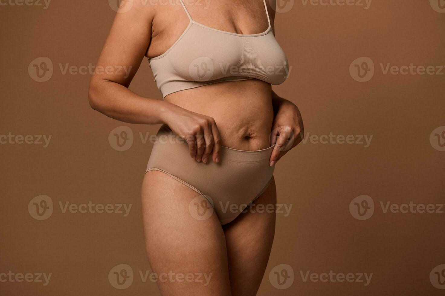 Close-up body of overweight woman with stretch marks and saggy belly after pregnancy, isolated on beige background with copy space for ads. Concept of love and acceptance, body positive. photo