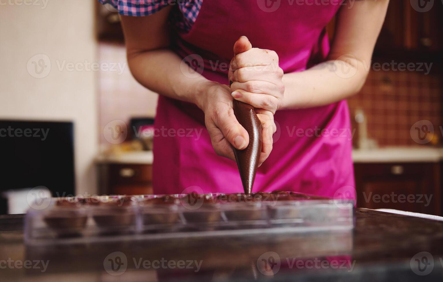 Cropped view of chocolatier pouring chocolate filling into chocolate mold preparing luxurious handmade pralines photo