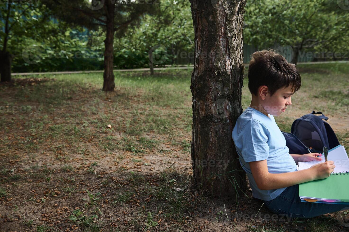 Side view of a Hispanic handsome teenager, school boy writing, making notes on copybooks, doing homework in the backyard photo