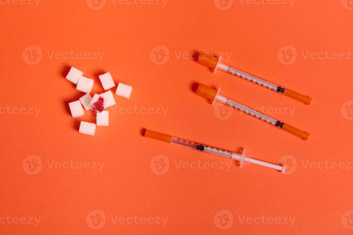 Flat lay composition of insulin syringes and white sugar cubes with blood drop isolated over colored orange background with copy space for medical ad. World diabetes day awareness concept, 14 November photo