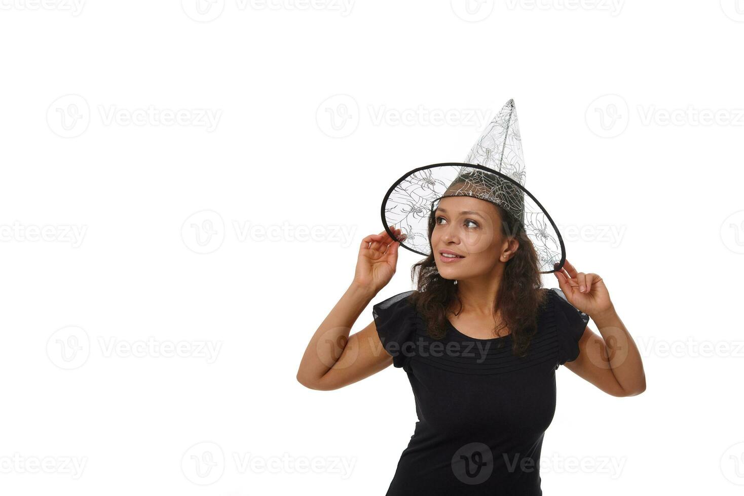 Isolated portrait on white background of an attractive young woman smiling with beautiful toothy smile, wearing a witch wizard hat and looking at the side on a copy space for Halloween advertisement photo