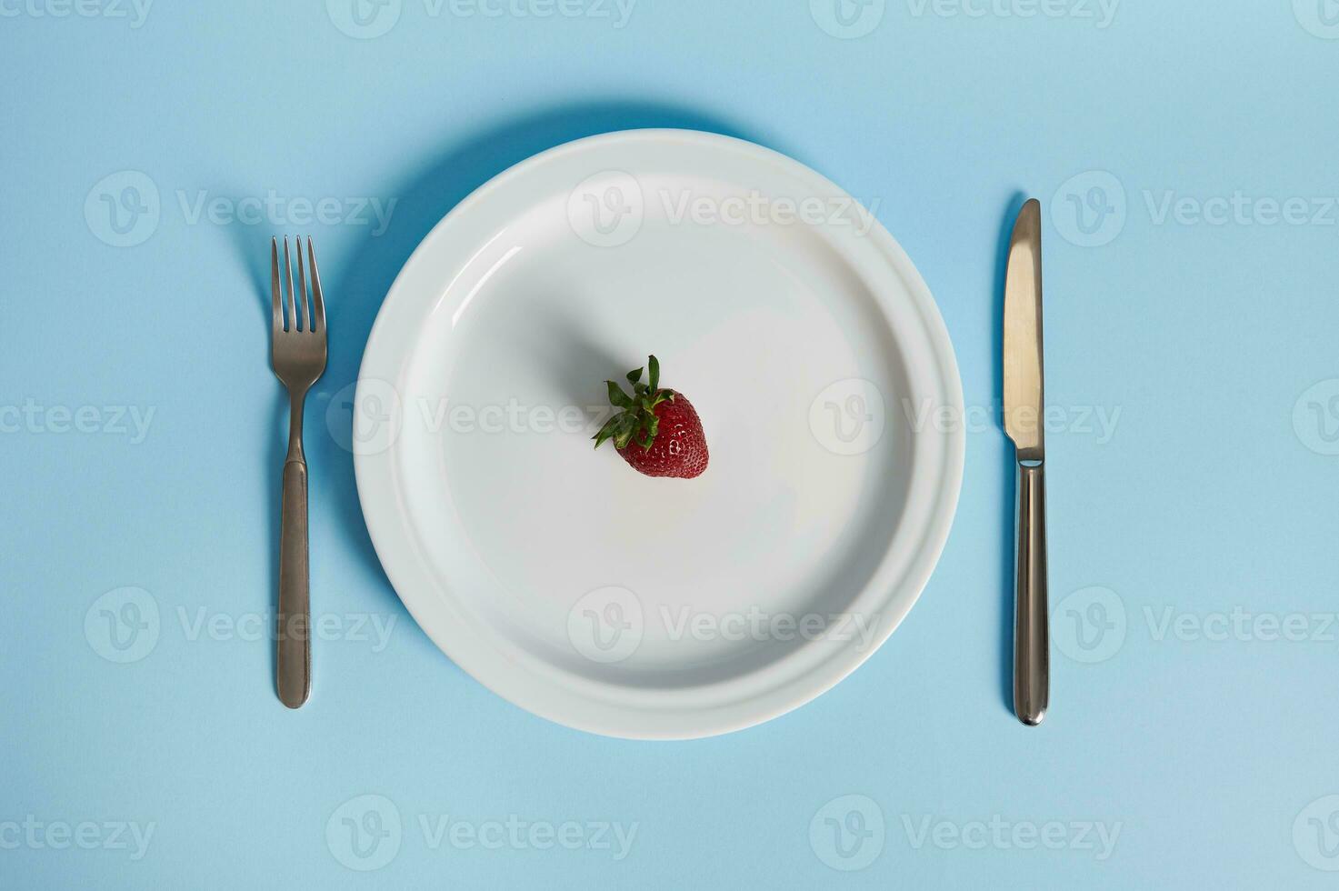 Flat lay composition with a delicious strawberry on a plate, fork and knife isolated on blue background. photo