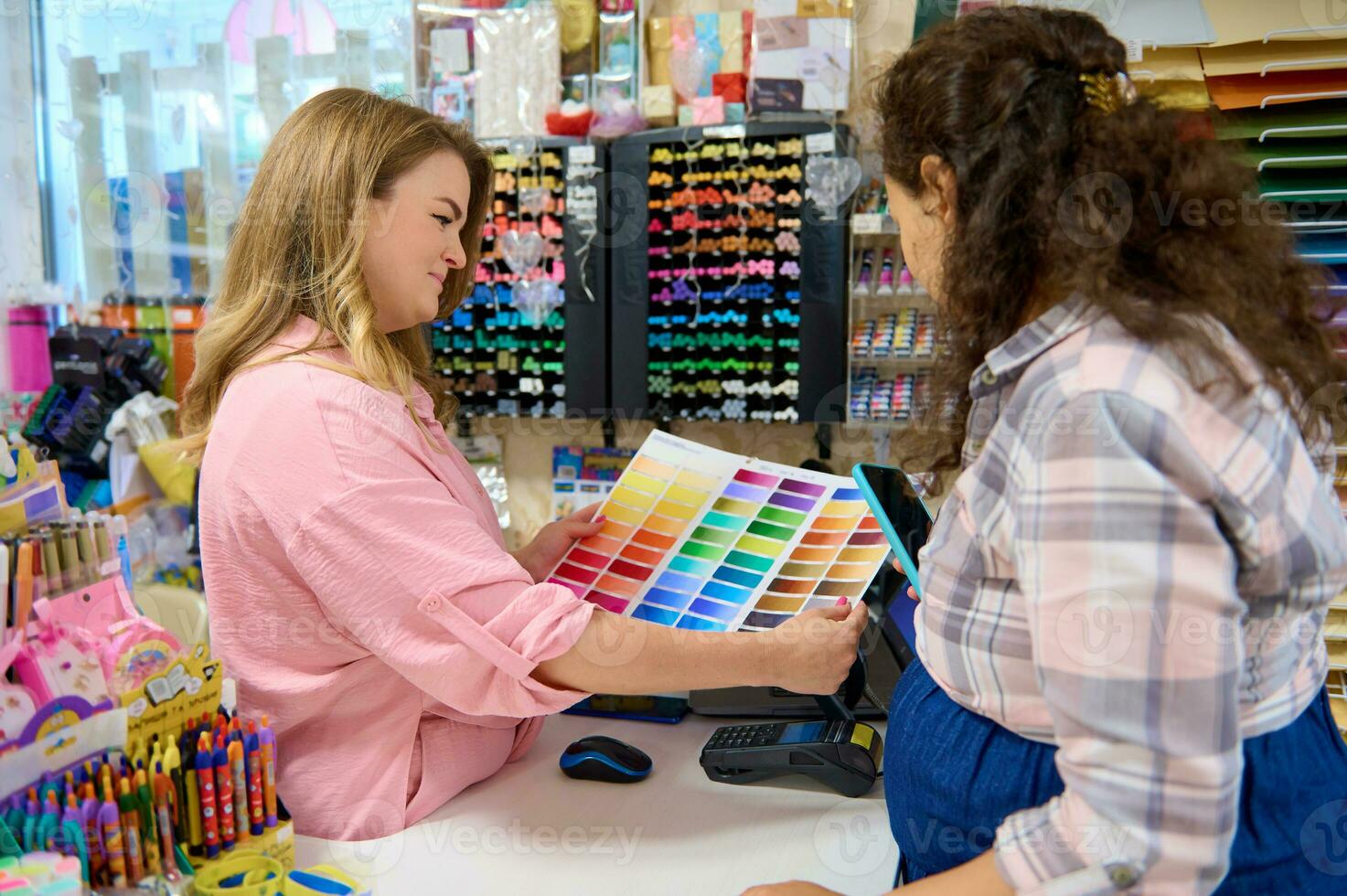 Saleswoman demonstrating a palette with color swatches of watercolor paints to customer shopping in a stationery store photo