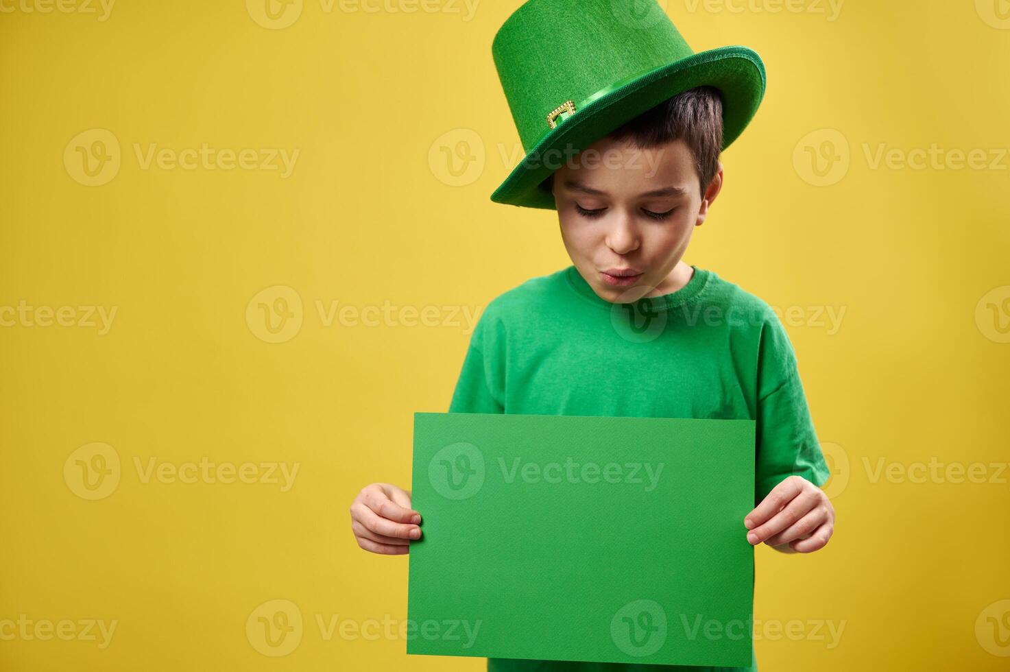 Little boy in green leprechaun hat looks at a green sheet of paper in his hands . Copy Space. St. Patrick's Day photo