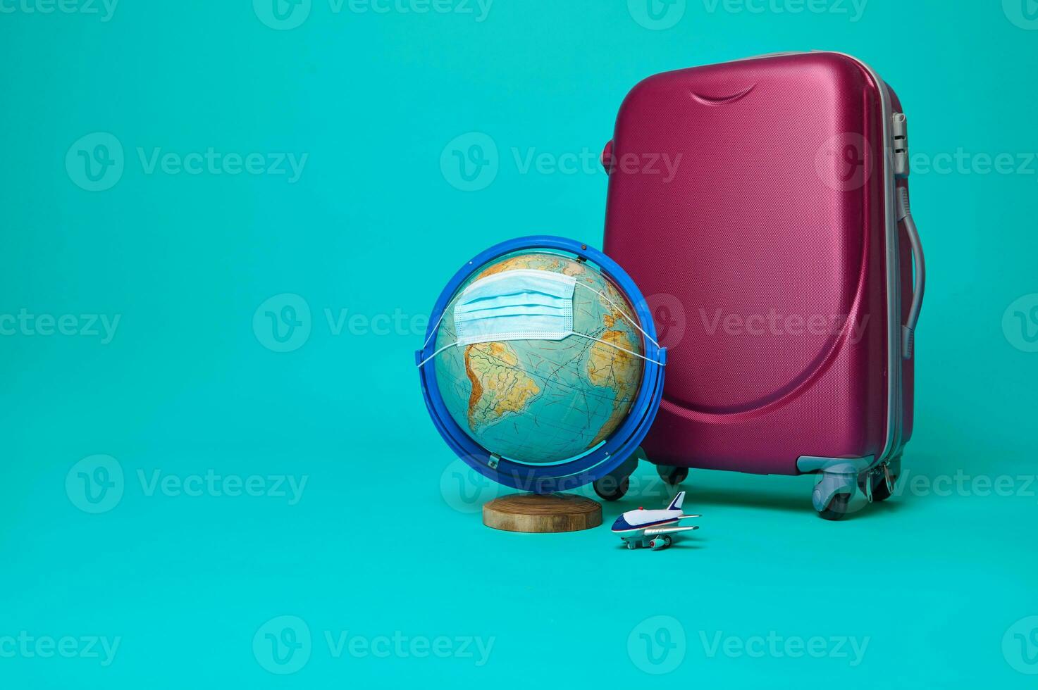 Suitcase, toy airplane, globe - planet Earth with protective medical mask isolated on blue background, copy space for advertising. Tourism and air travel safety concept during pandemic photo