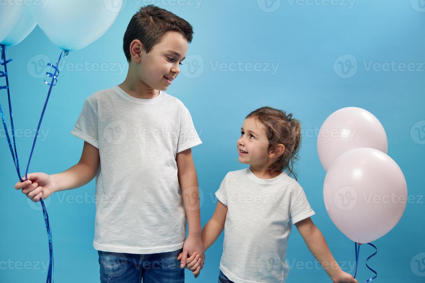 A boy and a girl are standing side by side, holding hands and looking tenderly at each other. Happy childhood photo