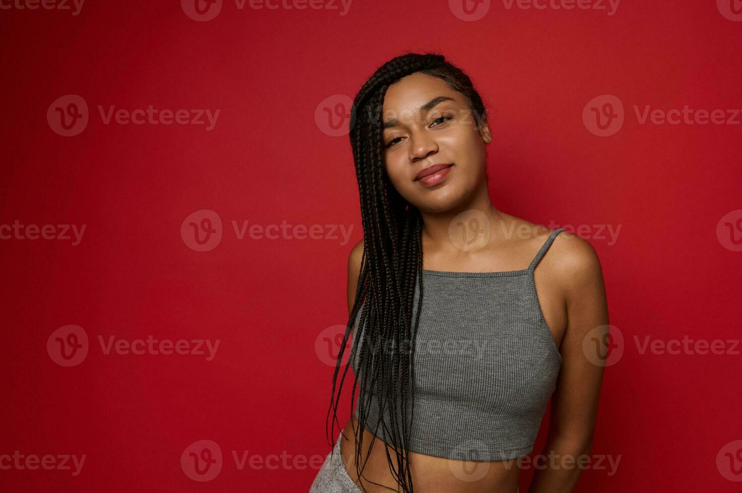 Young cute woman, attractive charming African American female athlete in gray sportswear posing against red colored background with copy space for ad photo