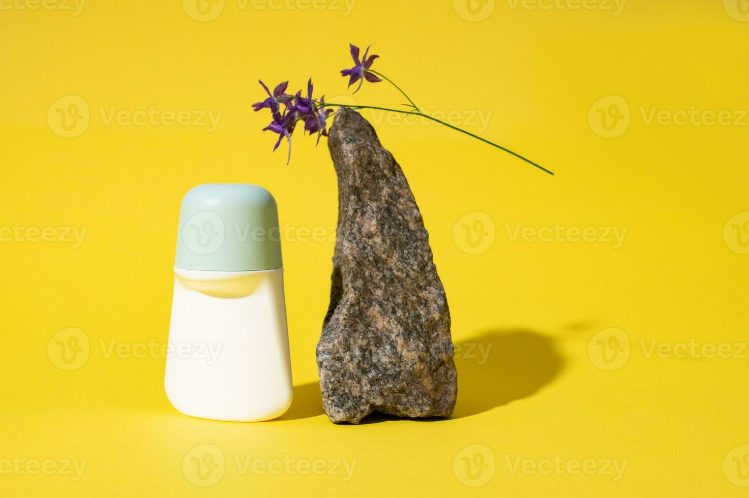 Still life with white mockup antiperspirant roller near a stone on a palm leaf, isolated on yellow studio background. photo