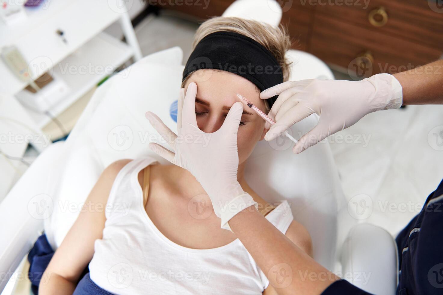 Top view of young woman receiving botulinum toxin injection into face. Anti-aging treatment, prevention of symptoms of the early aging process photo