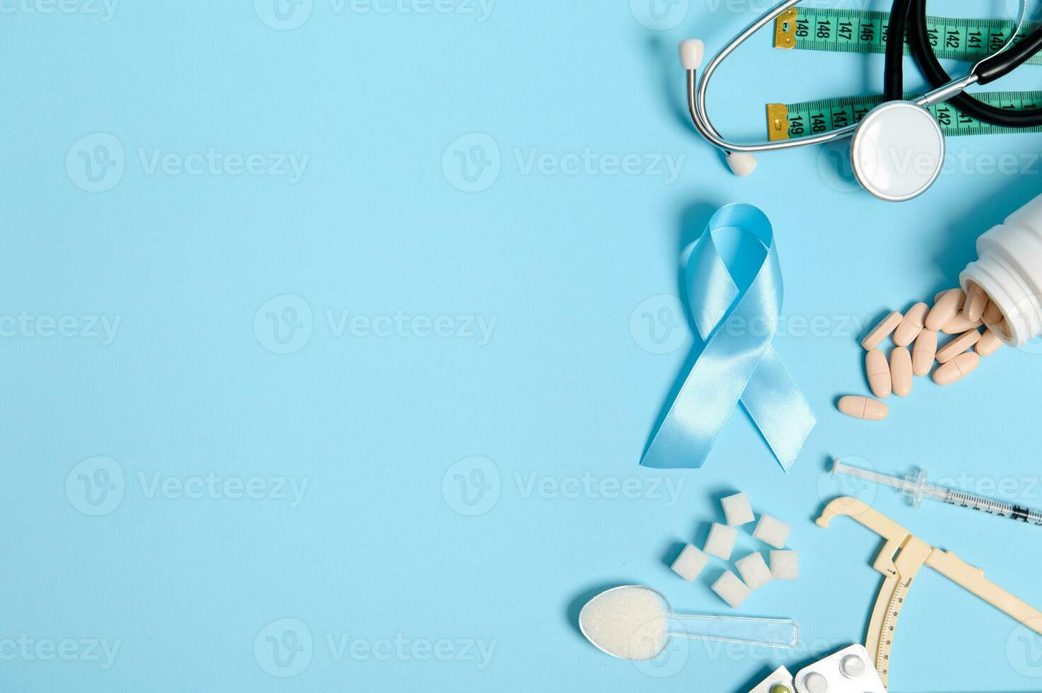 Scattered pharmaceutical pills, insulin syringe, stethoscope, caliper, measuring tape, refined white sugar and blue ribbon, symbol of Diabetes Awareness Day, on colored background with copy space. photo