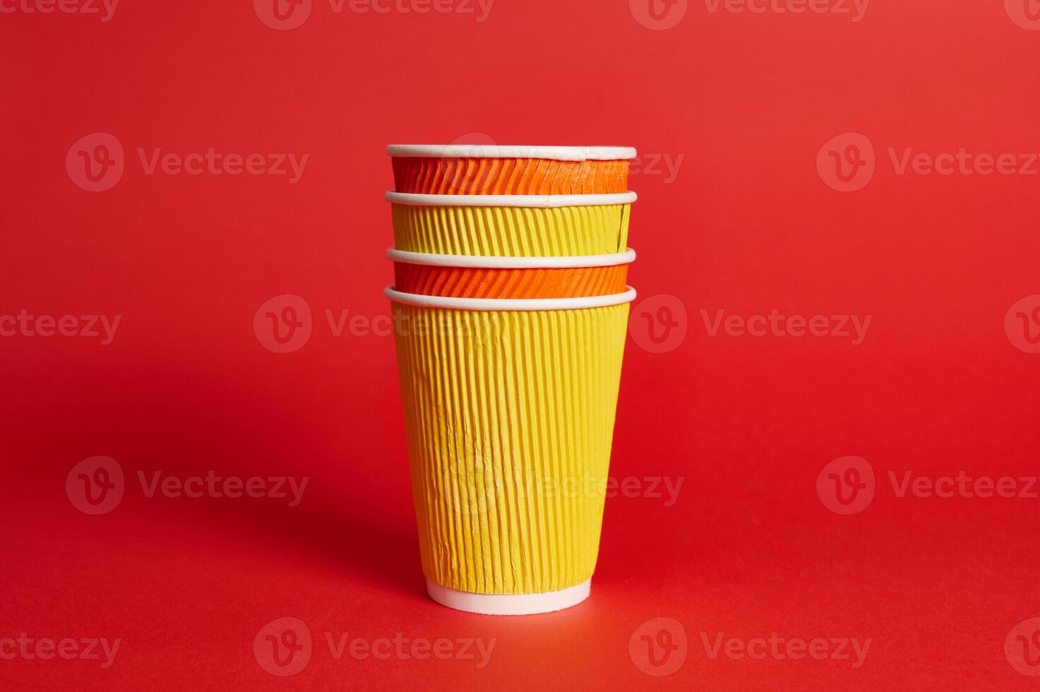 Stack of multicolored paper disposable cups for hot drinks on a red background with copy space. photo