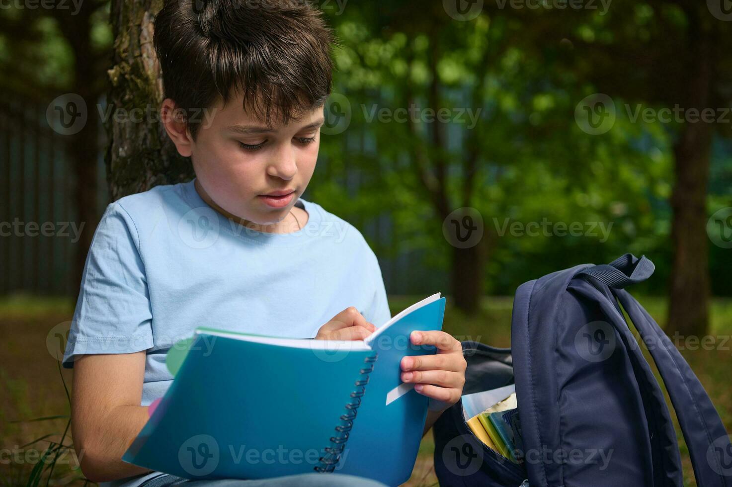 Close-up of Hispanic smart preteen school child boy writing on copybook, doing homework outdoors. Back to school concept photo