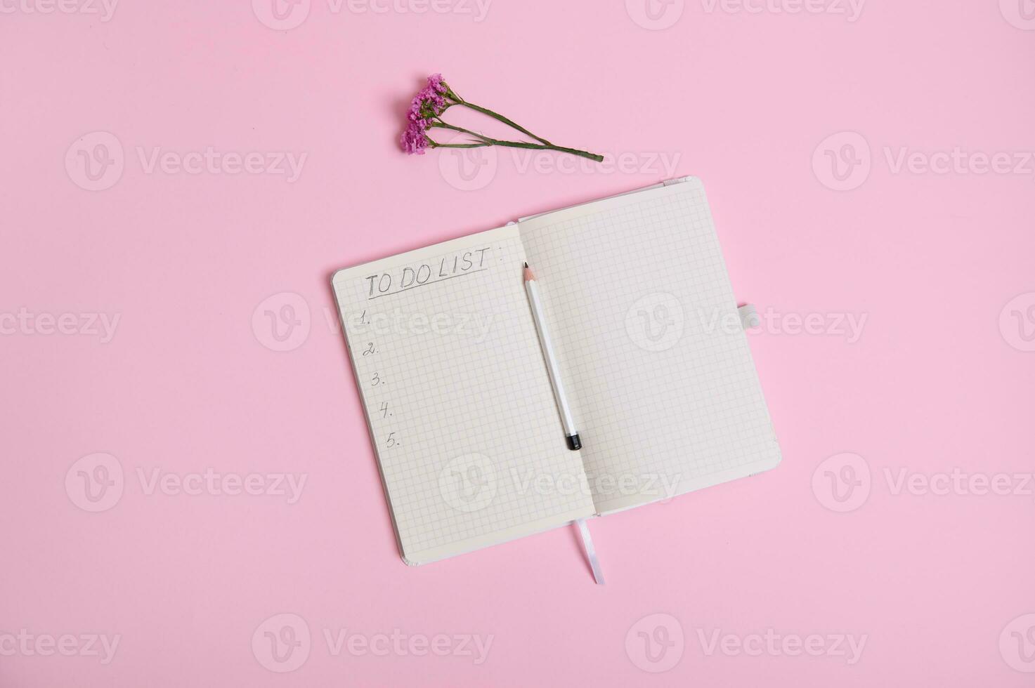Still life. Open agenda, diary, notebook with a list to do on white sheet of paper in line with copy space, pencil in the middle of the agenda and meadow flower on pink background with copy space photo